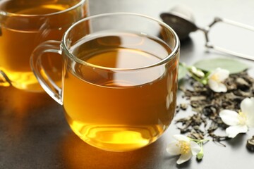 Aromatic jasmine tea in glass cups, brew and flowers on grey table, closeup