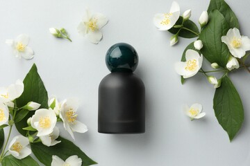 Bottle of perfume and jasmine flowers on light background, flat lay