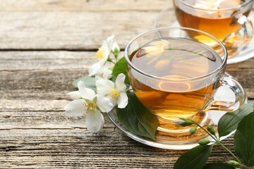 Aromatic jasmine tea in glass cups, flowers and green leaves on wooden table, closeup. Space for...