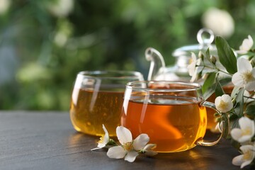 Tasty jasmine tea in cups, teapot and flowers on black table, closeup. Space for text