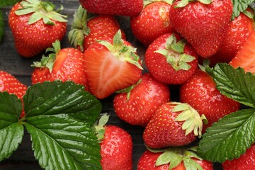 Fresh ripe strawberries and leaves on black wooden table, flat lay