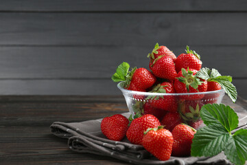 Fresh ripe strawberries and leaves in container on black wooden table, closeup. Space for text
