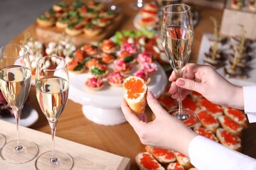 Buffet menu. Woman taking glass of sparkling wine and caviar sandwich from table, closeup
