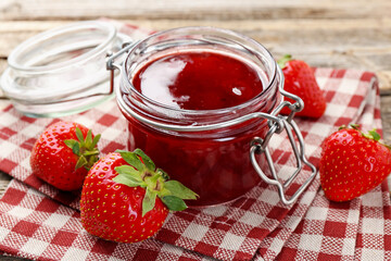 Tasty strawberry jam in glass jar and fresh berries on table, closeup
