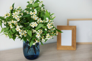 Beautiful jasmine flowers in vase and photo frames on wooden table indoors, closeup