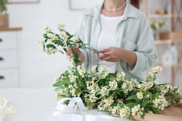 Woman making bouquet of jasmine branches at white table, closeup