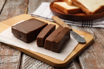 Tasty chocolate butter, slices of bread and knife on wooden table, closeup