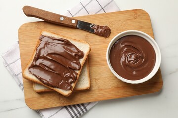 Tasty chocolate butter in bowl, slices of bread and knife on white marble table, top view