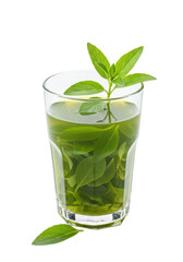 A clear glass holds liquid with vibrant green plant leaves, some floating at the top