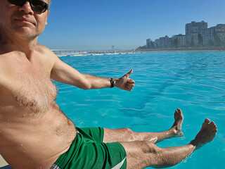 Man in a green shirt and shorts is sitting in a pool. He is giving a thumbs up in Cape Town in...
