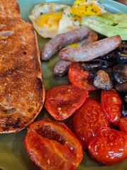 Plate of food with a piece of bread and a sausage. There are also tomatoes and mushrooms on the plate