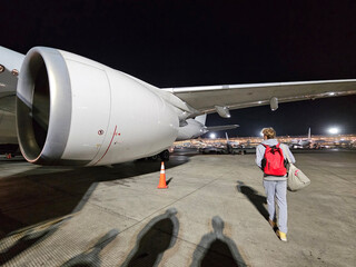 Person boy is walking on the ground next to an airplane. The airplane has a large jet engine on the...