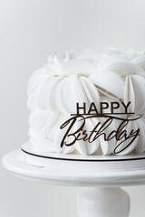 Birthday cake covered with white edible paper petals and decorated with golden Happy Birthday topper. White background