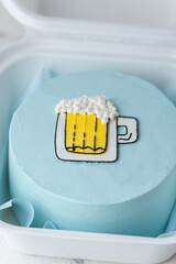 Small bento cake with blue cream cheese frosting decorated with a glass of foaming beer drawing in a gift box. Trendy cake as a gift for a beloved man