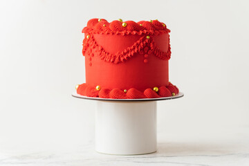 Delicate lambeth style birthday cake with red cream cheese frosting decorated with cream tracery and golden sprinkles. White background