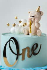 Birthday cake for a little one year old baby with blue chocolate frosting decorated with chocolate figure of teddy bear and white clouds. Baby shower cake for a little boy on turquoise background
