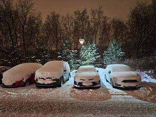 Row of cars are parked in a parking lot with snow on them. The cars are parked in a row, with the...