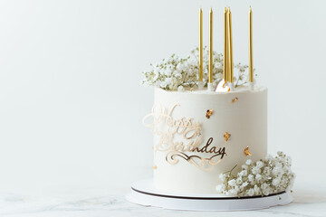 Beautiful white birthday cake decorated with golden candles and field  gypsophila flowers on the white background