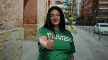 Woman volunteer smiling on city street giving thumbs up in green shirt suggesting positivity and...