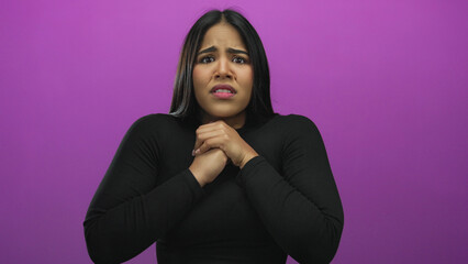 Fototapeta premium Young woman with dark hair and concerned expression, clasping hands on pink background, conveying anxiety and stress.