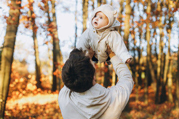 Happy father playing with cute baby son in soft evening light in autumn woods. Fatherhood. Stylish...
