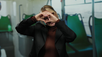 Woman smiling on a bus showing a heart gesture with her hands in a relaxed indoor setting