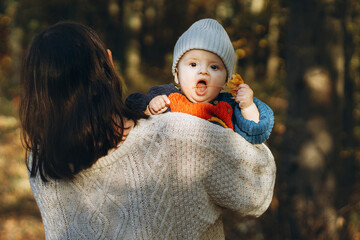 Happy mother hugging cute baby son in autumn woods. Motherhood. Stylish woman with adorable child in cozy warm sweaters embracing and relaxing in fall park