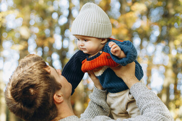 Happy father playing with cute baby son in autumn woods. Fatherhood. Stylish man with adorable child in cozy warm sweaters having fun and relaxing in fall park