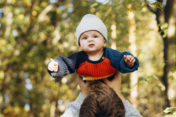 Cute baby son with funny emotions in father hands close up in autumn woods. Fatherhood. Stylish man with adorable child in cozy warm sweaters having fun and relaxing in fall park