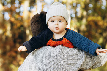 Cute happy baby son with funny emotions close up in father hands  in autumn woods. Fatherhood. Stylish man with adorable child in cozy warm sweaters relaxing in fall park
