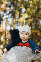 Cute happy baby son with funny emotions close up in father hands  in autumn woods. Fatherhood. Stylish man with adorable child in cozy warm sweaters relaxing in fall park