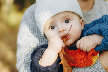 Cute baby son with funny emotions holding leaves close up in father hands  in autumn woods. Fatherhood. Stylish man with adorable child in cozy warm sweaters relaxing in fall park