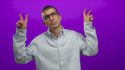 Caucasian man in glasses gesturing quotation marks on a vibrant purple background, isolated against...