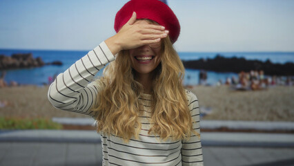 Woman holds a hand covering eyes against a beach backdrop while a blonde young figure is smiling...