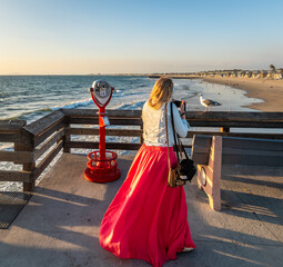 Woman with red skirt taking a photo of a seagull