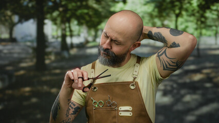 Man standing in a sunny park outdoors, wearing apron and holding scissors with a thoughtful...