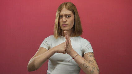 Young blonde woman hits bare palm with a clenched fist in a studio setting while frowning; anger...