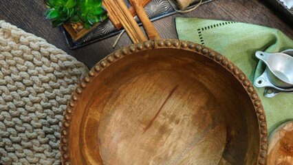 Empty wooden large mixing bowl surrounded by cinnamon sticks, pot holder, napkin and measuring...