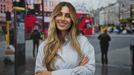 Fototapeta premium Young blonde woman wearing striped shirt arms crossed smiling at busy city bus stop; confidence friendliness.