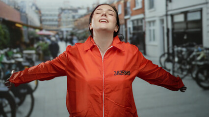 Woman smiling in orange prison jumpsuit embraces freedom outdoors on a vibrant urban street,...