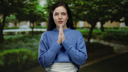 Woman meditating with closed eyes in a peaceful green park setting wearing a blue sweater outdoors...