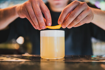 Bartender garnishing a cocktail with orange peel on a bar counter. Close-up shot highlights the...