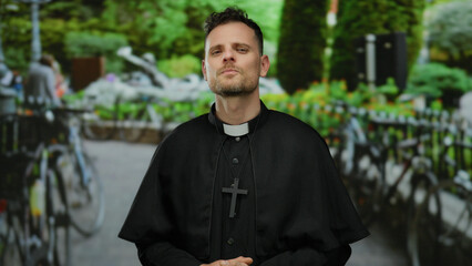 Priest standing in a lush green park setting with a solemn expression and religious attire,...