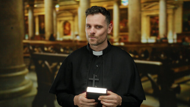 Priest smiling confidently indoors in a church setting, wearing black robe and cross necklace while holding a bible, signifying faith and religious devotion.