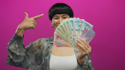 Woman holding hong kong dollars spread in hand against pink background showcasing money wealth...