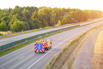 Road Maintenance Van with Warning Sign Driving on Empty Highway at Sunset