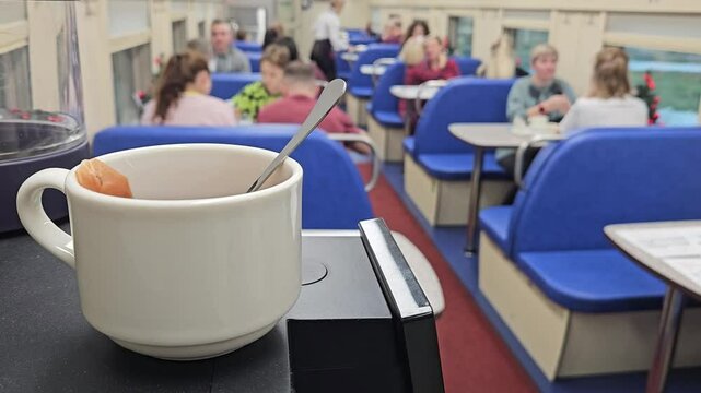 MOSCOW - DEC 25, 2023: White cup with a spoon in it sits on a counter. The cup is next to a machine that has a card reader in train restaurant dining car railroad transit connection on ground