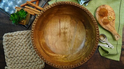 Empty wooden large mixing bowl surrounded by cinnamon sticks, pot holder, napkin and measuring...