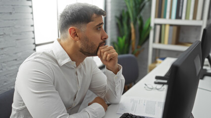 Young man in office thoughtfully working at computer in bright modern interior focusing intently...