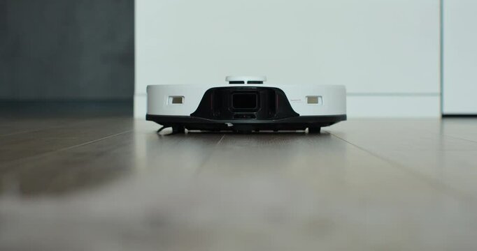The robot vacuum cleaner cleans the floor in the room. Close-up of a vacuum cleaner driving on the floor.